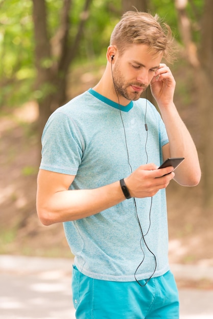 Muziek voor fitness Atletische man luistert naar muziek op smartphone Mobiele muziek Muziekmix ideaal voor krachtige cardiotraining Sport en actieve levensstijl Gezondheid en welzijn Buiten trainen