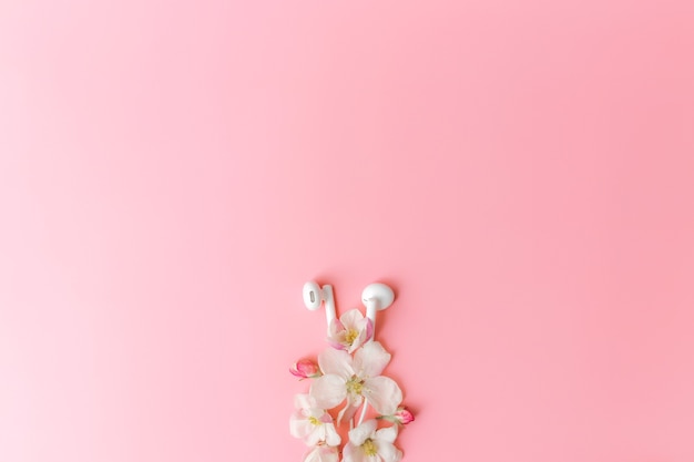 Muziekliefhebber of verse muziekconcept plat lag op roze achtergrond met appelbloesem en witte oortelefoons