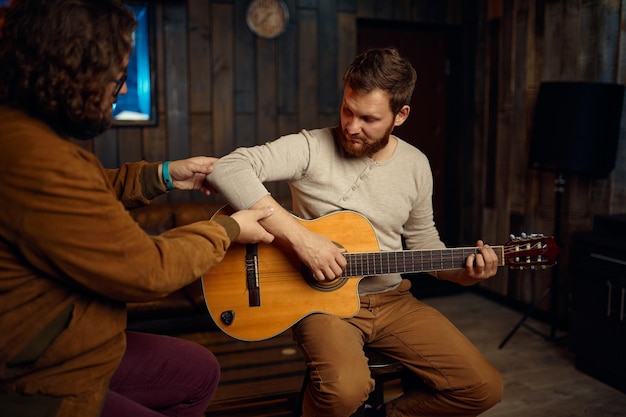 Muzikant die rechterhandpositie toont aan student. Guy verbetert zijn vaardigheden in het spelen van gitaar tijdens de les