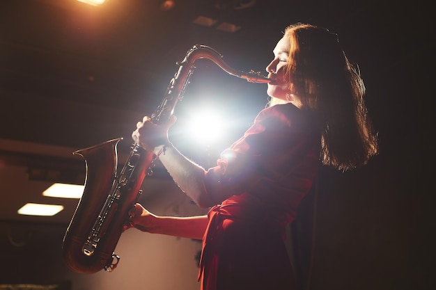 Muzikant meisje in een rode jurk met een saxofoon op het podium