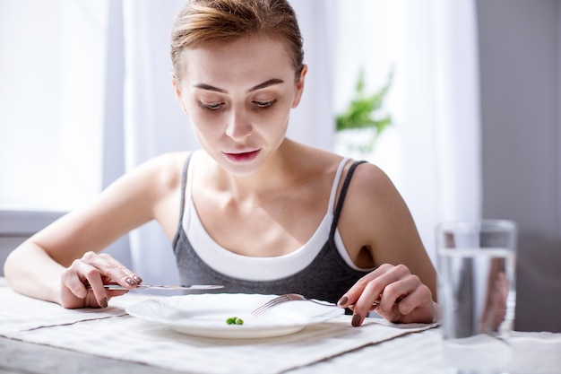 私の朝食。フォークとナイフを持ってエンドウ豆を見ている素敵な真面目な女性