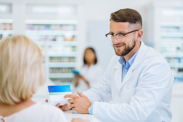 My client. Handsome pharmacist keeping smile on his face while looking at blonde woman