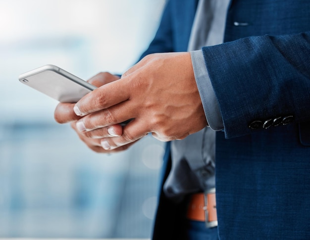 My clients know Im only a text away Cropped shot of an unrecognizable businessman standing alone in the office and using his cellphone