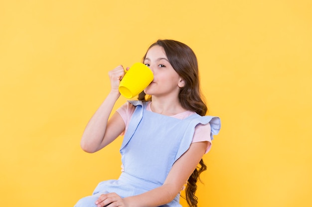 Not my cup of tea Making sip Drink enough water Girl kid hold mug yellow background Lovely child hold mug Drinking tea juice cocoa Relaxing with drink Child drink beverage Healthy habits