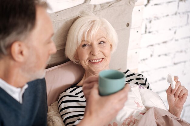 My darling. Smiling senior woman is going to take some hot drink from her loving husband.