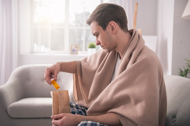 My delivery. Serious young man wearing a plaid while taking out the medicine from the bag