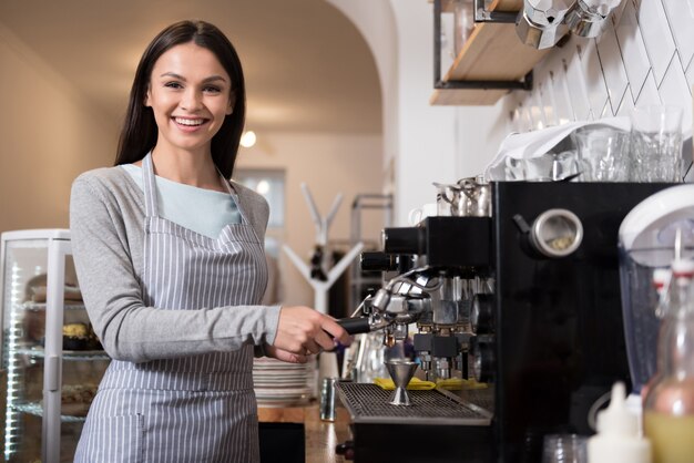 My favorite coffee. Cute beautiful woman smiling and using coffee machine while standing at the bar.