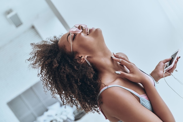 My favorite song! Attractive young African woman listening music and smiling while spending time at home