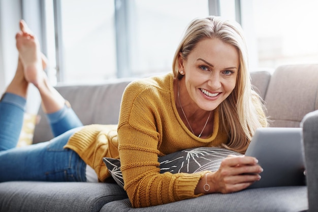 My go to gadget for downtime entertainment Portrait of an attractive mature woman using a digital tablet while relaxing on the sofa at home