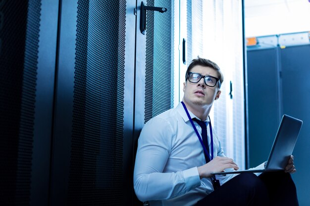 My good work. Determined serious man sitting on the floor and working on his laptop