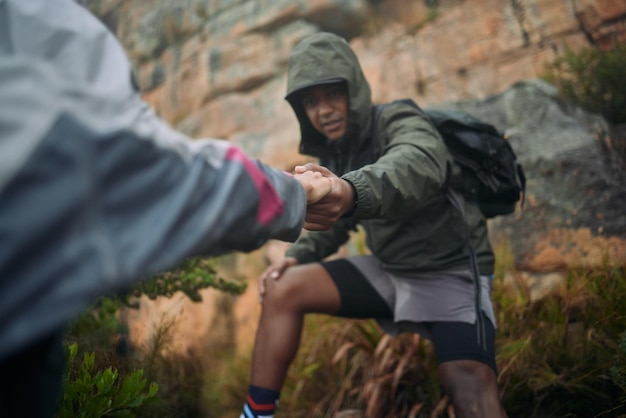 Photo my hand will always be there when you reach out for help shot of a man helping his partner up a cliff while mountain climbing