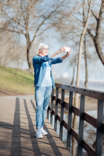 My hobby. Joyful old woman taking pictures while walking in the park