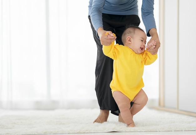 私の小さな女の子は最初の一歩を踏み出します。家族の幸せな小さな赤ちゃんが母親と一緒に歩くことを学ぶ