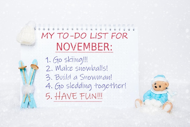 My November todo list Notepad with a todo list skiing making snowballs making a snowman sledding having fun and a toy Teddy bear in blue clothes blue skis white hat on white snow