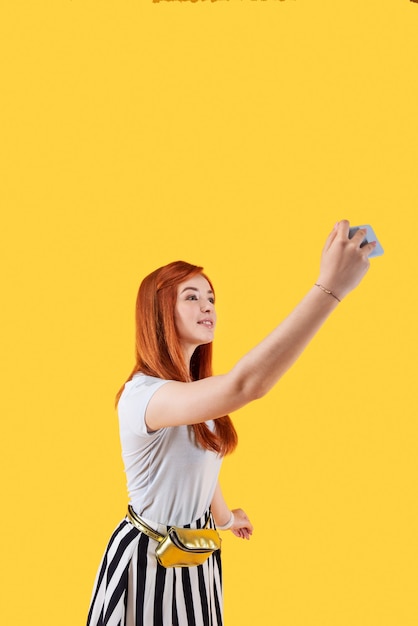 私の自撮り。セルフィーを撮りながらスマートフォンのカメラを覗き込んでいるポジティブな赤毛の女性