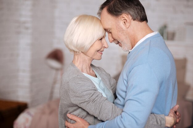 My sweetheart. Portrait of aged couple embracing and looking at each other while standing closely at home.