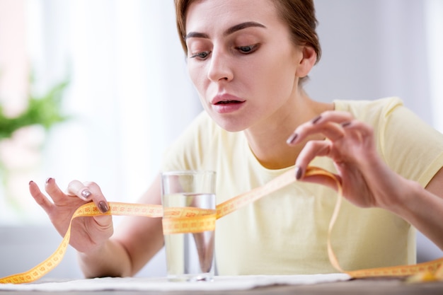 私の水。ガラスを測定しながらセンチメートルのテープを保持している素敵な若い女性