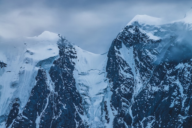 Mysterieus dramatisch berglandschap met besneeuwde bergtop in lage wolken in de schemering.