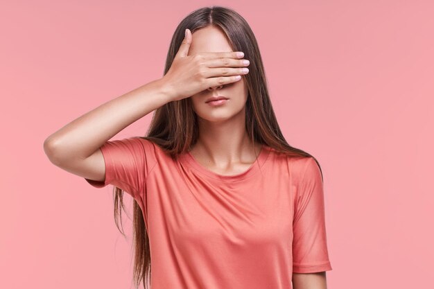 Mysterieuze jonge blanke vrouw draagt roze t-shirt en bedekt ogen met hand