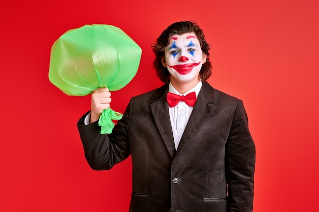 Mysterious magician holding inflated balloon in hands over red background, magician in black suit performing tricks