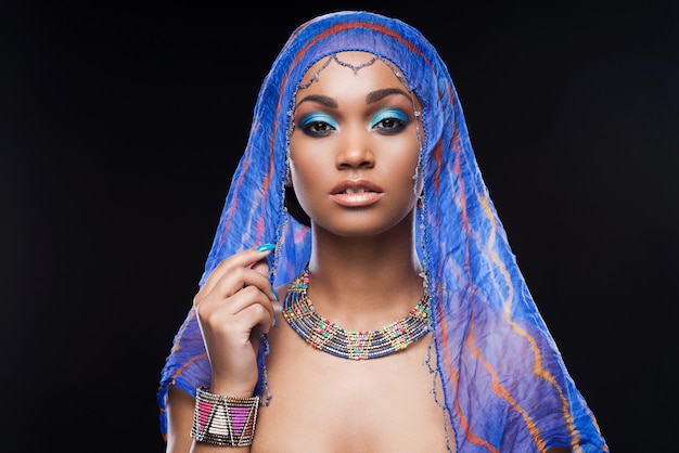 In mysterious style. Beautiful African woman covering head by scarf and looking at camera 