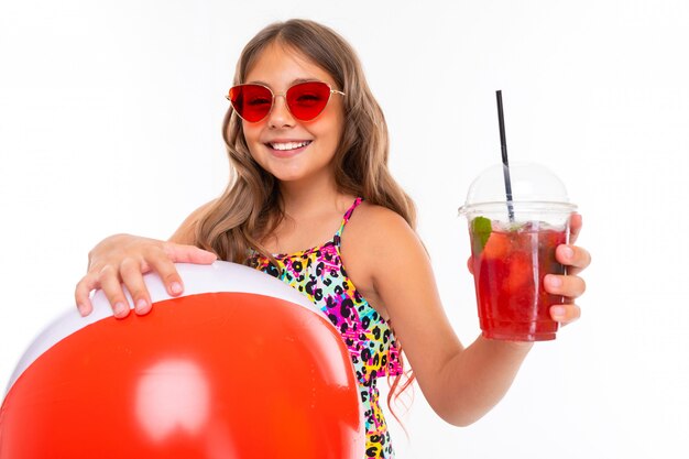  n attractive girl in a swimsuit with a ball and a cocktail on a white wall