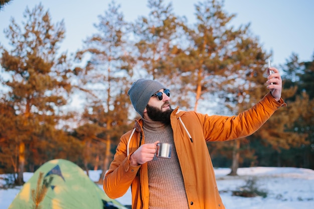 Na de beklimming bewondert de toerist de zonsondergang terwijl hij bij de tent staat met een kopje thee of koffie en maakt een foto op zijn telefoon