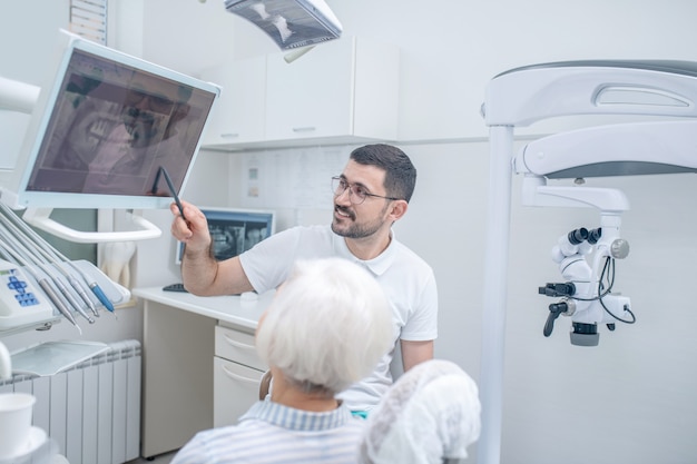 Na röntgenfoto. Mannelijke jonge tandarts die de resultaten van xray toont aan zijn vrouwelijke patiënt