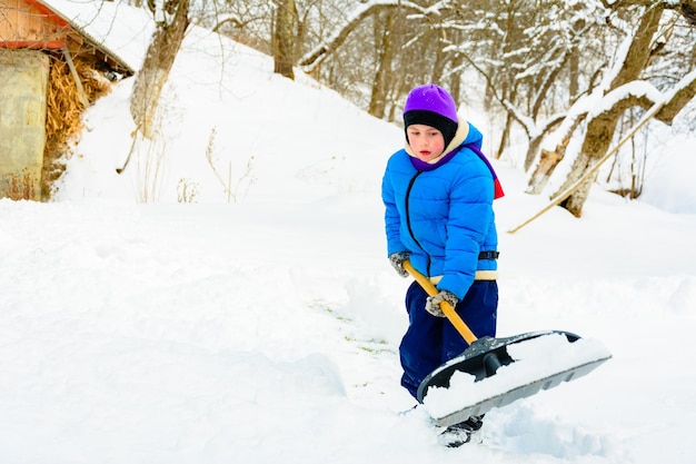 Na zware sneeuwval ruimt de kleine jongen de sneeuw met een schop