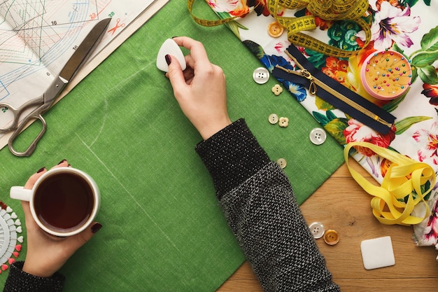 Naaiatelier of modeontwerper aan het werk. Bovenaanzicht op vrouwelijke handen die doekvierkant markeren met stuk zeep. Rommelige tafel met naaiaccessoires en patronen, kopieer ruimte