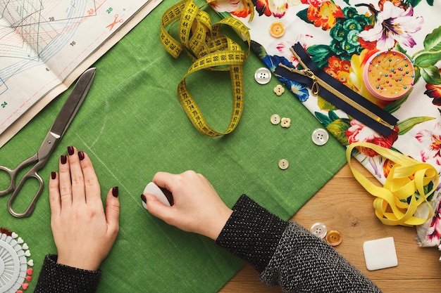 Naaiatelier of modeontwerper aan het werk. Bovenaanzicht op vrouwelijke handen die doekvierkant markeren met stuk zeep. Rommelige tafel met naaiaccessoires en patronen, kopieer ruimte