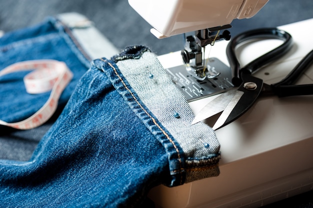 Naaien indigo denim jeans met naaimachine, kledingstuk industrieel concept.