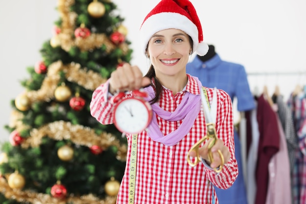 Naaister in rode kerstmuts met wekker en schaar in de buurt van kerstboom