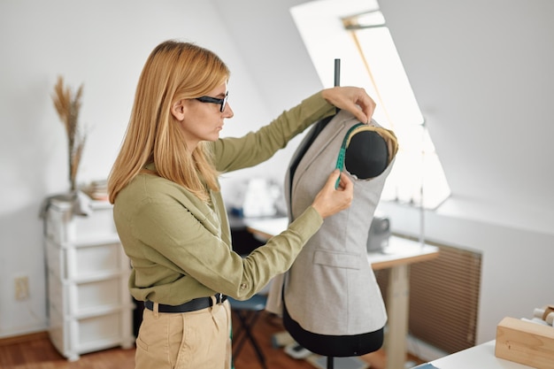 Naaister meet jurk op etalagepop in werkplaats. Kleermakerij beroep en professioneel naaien, handgemaakte kleermakerij, ambachtelijke hobby