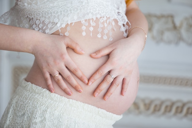 Naakte buik van een zwangere vrouw die haar handen in de vorm van een hart legde