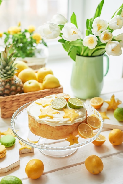 Foto naakte cake met citroenen en limoenen, fruit en witte tulpen