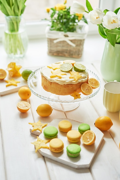 Naakte cake met citroenen en limoenen, zoete macarons en bloemen in vaas