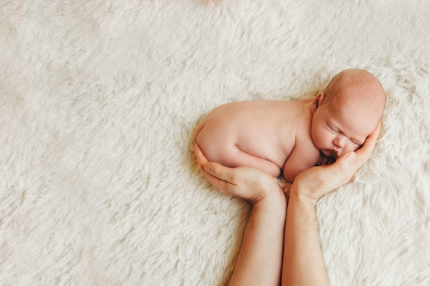 Naakte pasgeboren baby die op de handen van ouders op een wit ligt.