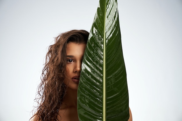 Naakte vrouw verbergt gezicht achter groot groen blad