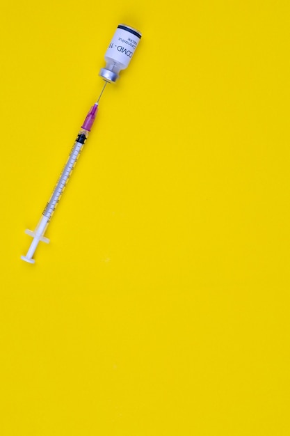 Foto naald van injectiespuitinzetstuk in fles covid-19 coronavirusvaccin op gele achtergrond met kopieerruimte. bovenaanzicht schot.