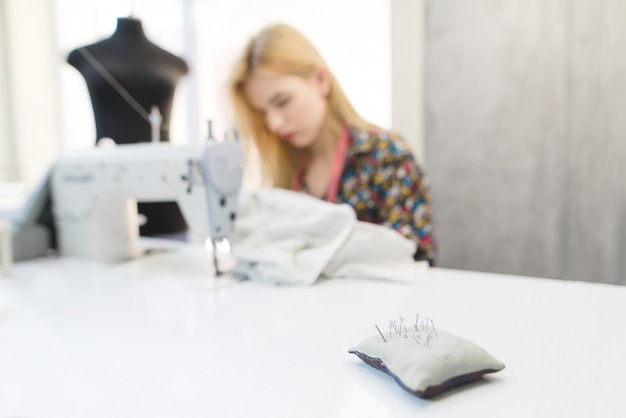 Naalden in een kussen op de achtergrond van naaisters bezig met een naaimachine