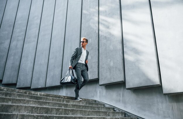 Naar beneden gaan bij de trap Jonge zakenman in grijze formele kleding is buiten in de stad