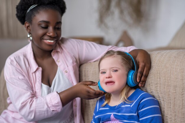 Naar muziek aan het luisteren. Afrikaanse Amerikaanse vrouw die hoofdtelefoons op het hoofd van een meisje zet