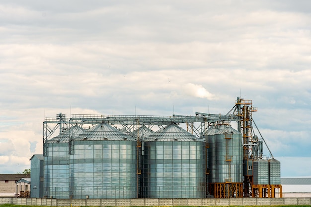 Naast het geploegde landbouwveld zijn zilveren silo's geïnstalleerd op een agro-fabriek voor verwerking, drogen, schoonmaken en opslag van landbouwproducten, meel, granen en graan Graanschuurlift