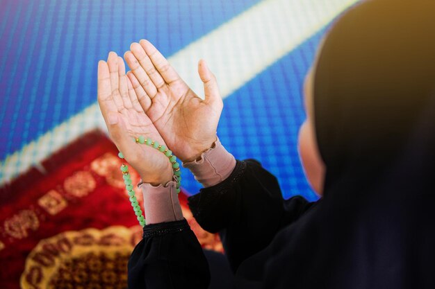 Foto nabijbeeld van een moslimvrouw die tot allah bidt met haar handen omhoog op een gebedsmat met kralen in haar hand