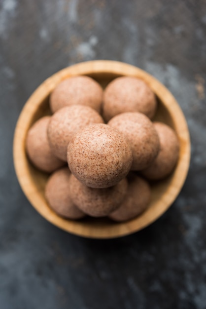 Nachni laddu or Ragi laddoo or balls made using  finger millet, sugar and ghee. It's a healthy food from India. Served in a bowl or plate with raw whole and powder. Selective focus