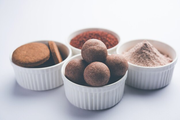 Photo nachni or ragi laddu and biscuits or cookies made using  finger millet, sugar and ghee. it's a healthy food from india. served in a bowl or plate with raw whole and powder