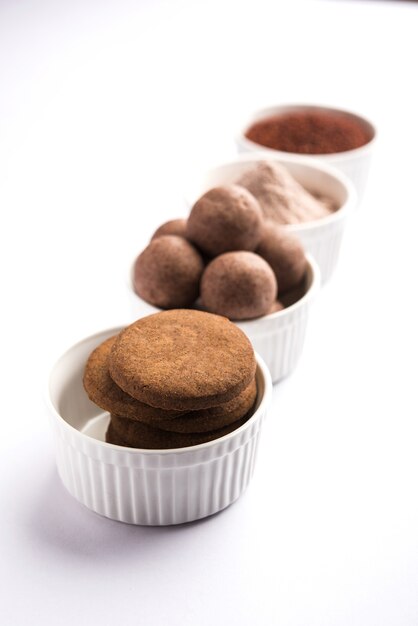 Nachni or Ragi laddu and biscuits or cookies made using  finger millet, sugar and ghee. It's a healthy food from India. Served in a bowl or plate with raw whole and powder