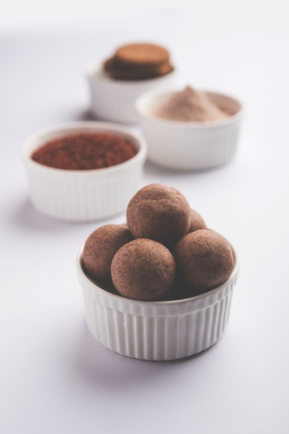 Nachni 또는 Ragi laddu 및 손가락 기장, 설탕 및 버터 기름을 사용하여 만든 비스킷 또는 쿠키. 인도에서 온 건강식입니다. 생 전체 및 분말과 함께 그릇이나 접시에 제공