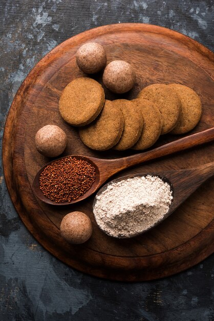 Nachni 또는 Ragi laddu 및 비스킷 또는 손가락 기장, 설탕 및 버터 기름을 사용하여 만든 쿠키. 인도에서 온 건강식입니다. 생 전체 및 분말과 함께 그릇이나 접시에 제공